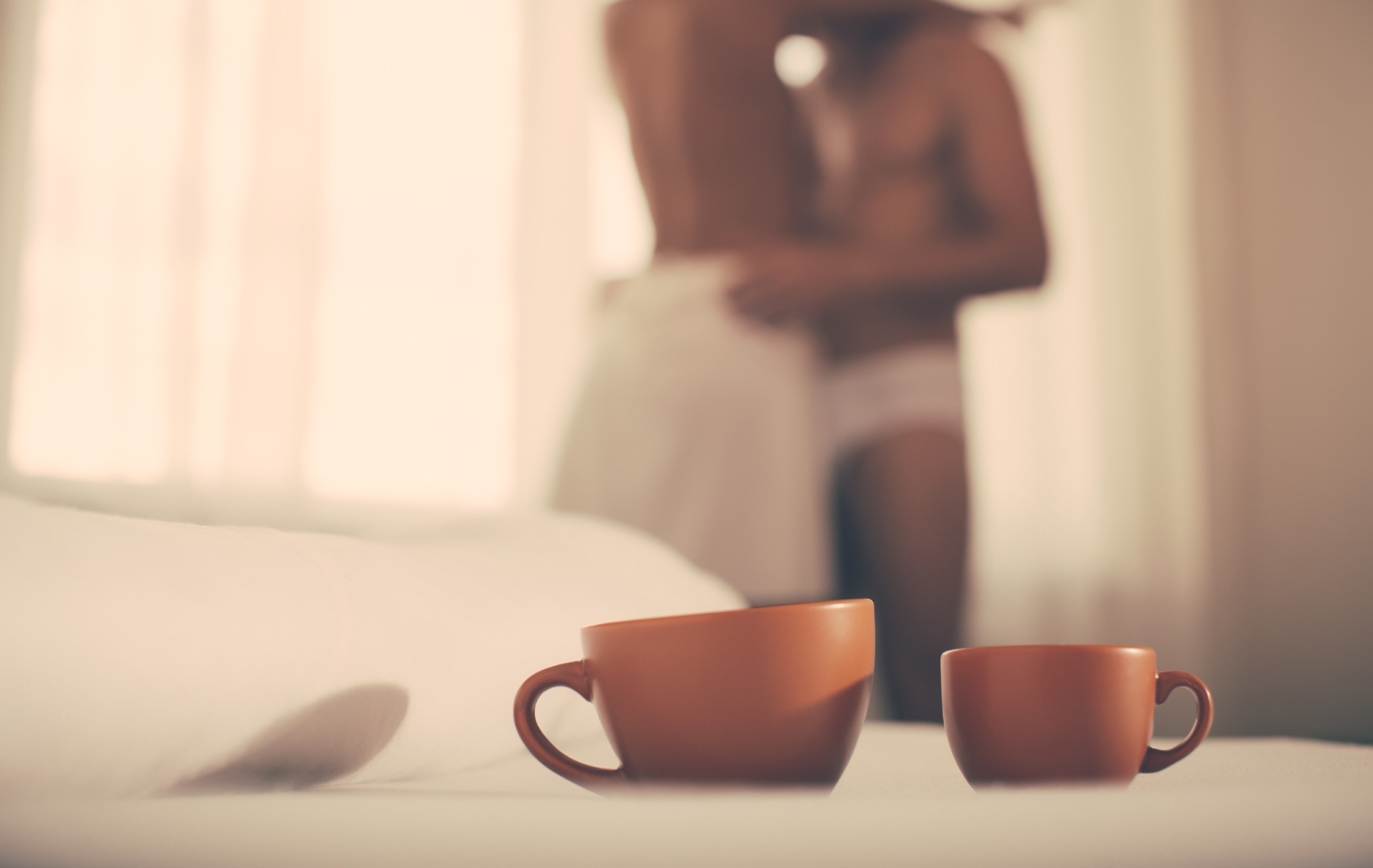 Two coffee cups with a couple embracing in the background